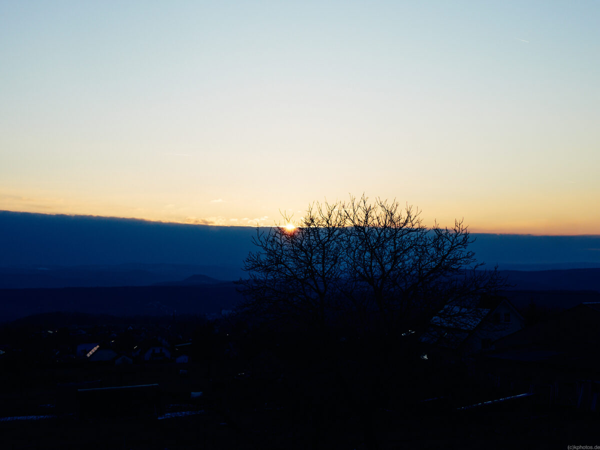 A sunset picture in which the sun disappears behind a dark cloud and only a little can be seen